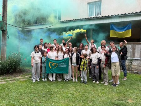 Een groep mensen staat in een grasveld met een Oekraïense vlag op de achtergrond